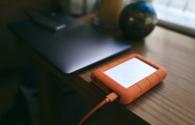 An external hard drive backup device connected to a laptop on a wooden table with a blurred background.